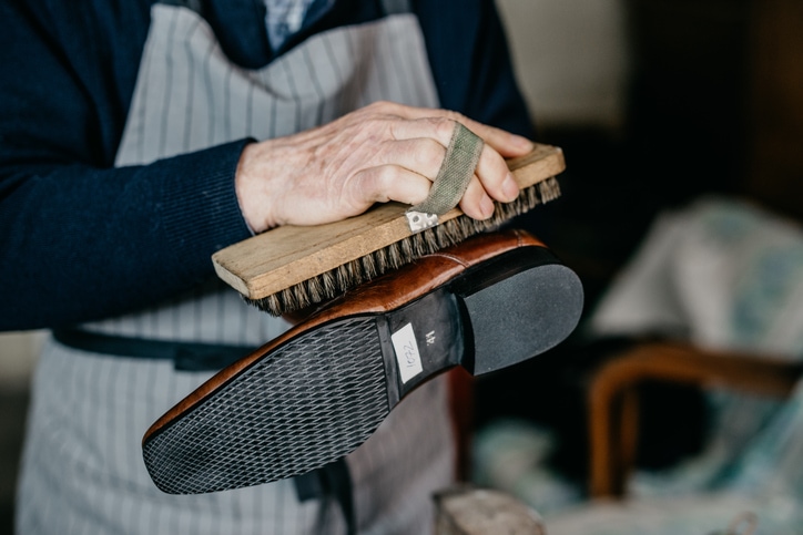 Old shoemaker is polishing a shoe