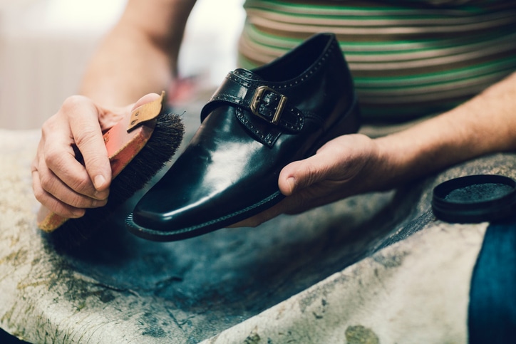 Unrecognizable Shoemaker polishing old shoes. Selective focus to brush.